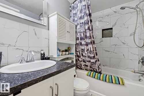 Bathroom featuring a white bathtub, a tiled shower surround with a recessed niche, and a vanity with a dark countertop and an undermount sink - 15 10164 150 Street, Edmonton, AB 