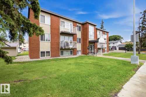 Brick and stucco multi-level building featuring multiple balconies with white railings, a concrete sidewalk, and a manicured lawn - 15 10164 150 Street, Edmonton, AB 