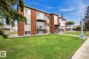 Brick and stucco multi-level building featuring multiple balconies with white railings, a concrete sidewalk, and a manicured lawn - 15 10164 150 Street, Edmonton, AB 