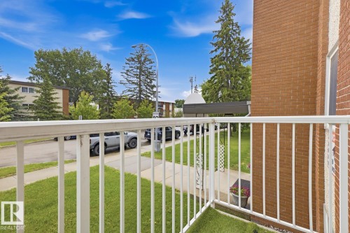 Balcony with white metal railing, artificial turf flooring, and a brick exterior wall - 15 10164 150 Street, Edmonton, AB 