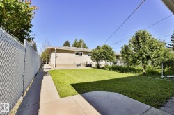 Expansive rear yard featuring a manicured lawn, established trees, concrete patio, and a side walkway - 