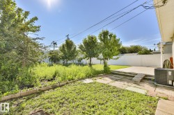 Expansive backyard featuring a concrete patio, a grass lawn, and mature trees - 