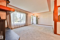 Spacious living area featuring a large picture window, an entryway with a panel door and transom window, a built-in fireplace with a stone hearth and wood mantel, and carpet flooring - 