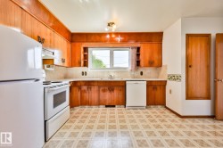 Kitchen featuring wood cabinetry, white appliances, a window above the sink, light-toned countertops, and patterned floor tiling - 