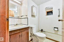 Bathroom featuring a wood-finish vanity with an integrated sink, white tiled backsplash with black trim, and a wall-mounted mirror - 