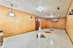 Spacious room featuring wood paneling, a patterned acoustic tile ceiling, and white square floor tiles with accent squares - 