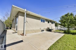 Rear exterior featuring stucco siding, white window trim, a concrete patio, and a grass lawn - 