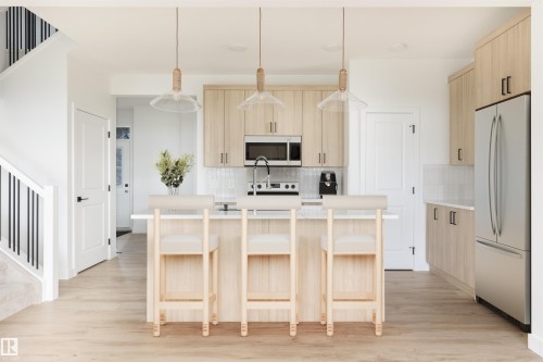Kitchen featuring light wood-finish cabinetry, stainless steel appliances, white tile backsplash, and a central island with countertop seating - 47 Chartres Close, St. Albert, AB 
