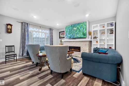 Living space featuring wood-finish flooring, recessed lighting, and a linear electric fireplace with a stacked stone surround - 1603 158 Street, Edmonton, AB 
