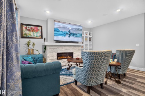 Living space featuring a stacked stone fireplace with an integrated linear electric insert, recessed lighting, and wood-finish flooring - 1603 158 Street, Edmonton, AB 