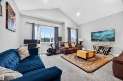 Vaulted ceilings enhance this spacious living area, featuring light gray walls and plush carpeting - 