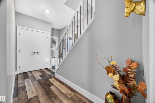 Entryway featuring wood-finish flooring, white paneled double doors, and a staircase with white risers and dark metal balusters - 1603 158 Street, Edmonton, AB 