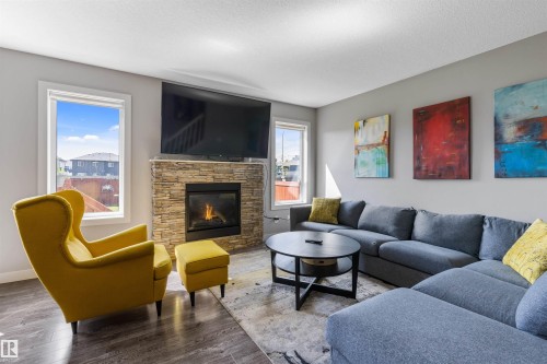 Living area featuring a floor-to-ceiling stacked stone fireplace, wood-finish flooring, and multiple windows - 1651 Hammond Crescent, Edmonton, AB 
