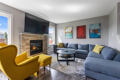 Living area featuring a stone-faced fireplace with a black insert, wood-finish flooring, and multiple windows - 1651 Hammond Crescent, Edmonton, AB 