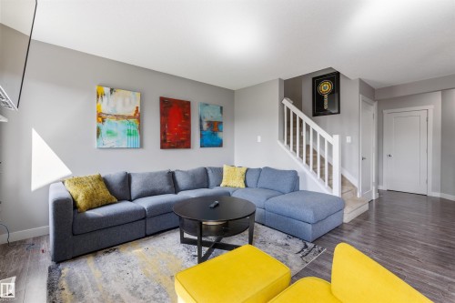 Open concept living space featuring wood-finish flooring, light gray wall tones, and a white staircase with carpeted treads - 1651 Hammond Crescent, Edmonton, AB 
