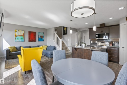 Open-concept living space featuring wood-finish flooring, a kitchen island with stone countertop, stainless steel appliances, and dark wood cabinetry - 1651 Hammond Crescent, Edmonton, AB 