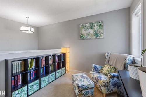 Carpeted loft area featuring a large window, a built-in bookshelf, a contemporary pendant light fixture, and light gray wall paint - 1651 Hammond Crescent, Edmonton, AB 