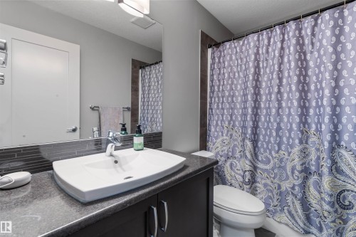 Contemporary bathroom featuring a dark vanity with a rectangular countertop sink, chrome faucet, and full-width mirror - 1651 Hammond Crescent, Edmonton, AB 