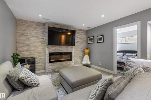Living area featuring a stone veneer accent wall, built-in electric fireplace, recessed lighting, and light wood-finish flooring - 1651 Hammond Crescent, Edmonton, AB 