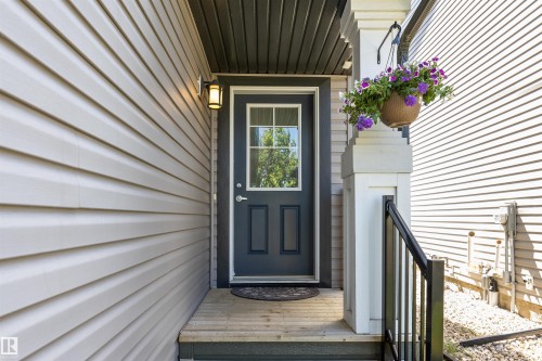 Front entry featuring a dark gray door with windowpanes, wood steps, and a black metal handrail - 1651 Hammond Crescent, Edmonton, AB 