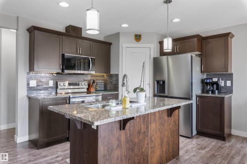 Kitchen featuring a large central island with granite countertop and undermount sink, dark wood-finish cabinetry, stainless steel appliances, and wood-finish flooring - 1651 Hammond Crescent, Edmonton, AB 