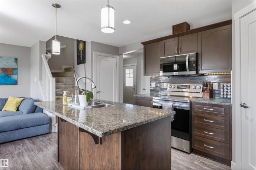 Kitchen featuring an island with a granite-style countertop, stainless steel appliances, dark wood-finish cabinetry, and a tile backsplash - 1651 Hammond Crescent, Edmonton, AB 