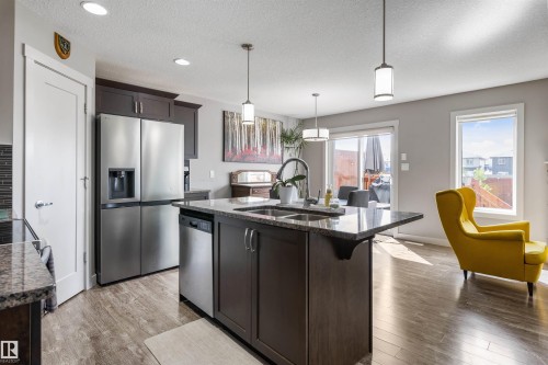 Modern kitchen featuring a central island with a double basin sink, stainless steel appliances, dark wood cabinetry, and granite countertops - 1651 Hammond Crescent, Edmonton, AB 
