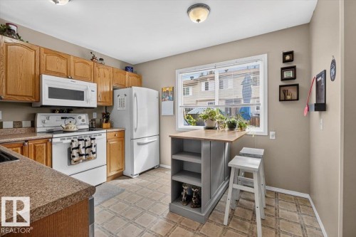 Kitchen featuring wood cabinetry, a window, integrated appliances, a breakfast bar, and patterned flooring - 27 Walden Park, St. Albert, AB 