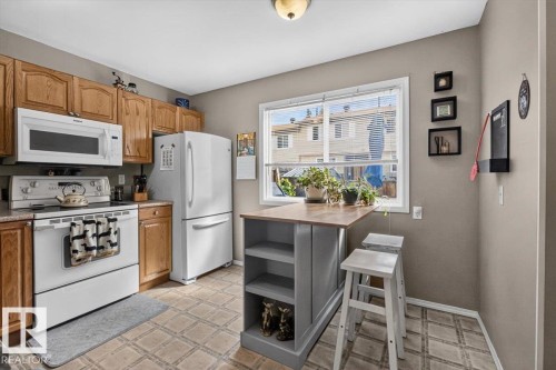 Kitchen featuring light wood cabinetry, white appliances, a center island with open shelving, and a dual-pane window - 27 Walden Park, St. Albert, AB 