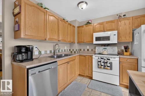 Kitchen featuring wood cabinetry, laminate countertops, a tile backsplash, a stainless steel dishwasher, and a white electric range with an over-the-range microwave - 27 Walden Park, St. Albert, AB 