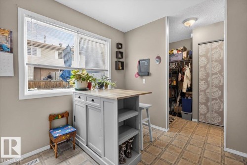 Kitchen area featuring a light-toned wood-finish island with integrated storage, a double window with blinds, and patterned flooring - 27 Walden Park, St. Albert, AB 