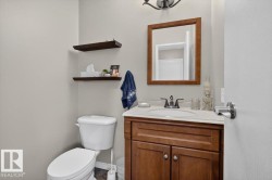 Powder room featuring a wood vanity with a white countertop and integrated sink, a wood-framed mirror, and two floating wood shelves - 
