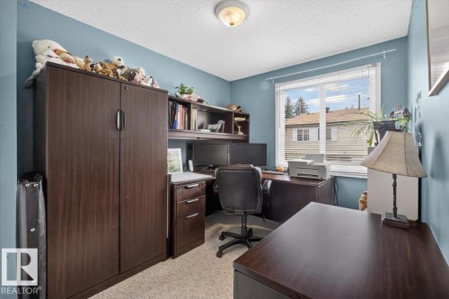 Well-lit room featuring neutral carpet flooring, a large window with blinds, and a built-in office furniture system with a hutch and filing cabinet - 27 Walden Park, St. Albert, AB 