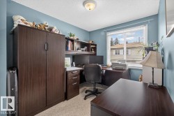 Well-lit room featuring neutral carpet flooring, a large window with blinds, and a built-in office furniture system with a hutch and filing cabinet - 