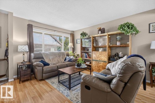 Living area featuring light wood-finish flooring, a large window with blinds, and neutral-toned walls - 27 Walden Park, St. Albert, AB 