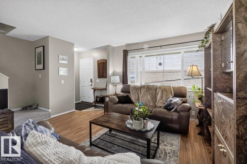 Living area featuring wood-finish flooring, a large window with blinds, and neutral wall tones - 27 Walden Park, St. Albert, AB 