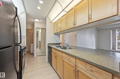 Kitchen featuring light wood cabinetry, stone-finish countertops, and a double basin stainless steel sink - 314 2430 Guardian Road, Edmonton, AB 