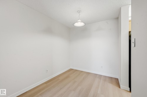 Compact interior space featuring wood-finish flooring, white baseboards, and a contemporary pendant light fixture - 314 2430 Guardian Road, Edmonton, AB 