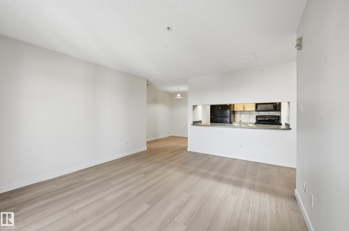 Open-concept living area featuring wood-finish flooring, white baseboards, and a pass-through window to the kitchen - 314 2430 Guardian Road, Edmonton, AB 