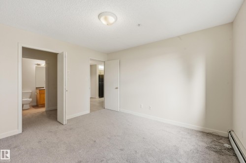 Carpeted interior room featuring light-toned walls, a textured ceiling, and a flush mount ceiling light - 314 2430 Guardian Road, Edmonton, AB 