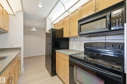 Kitchen featuring wood cabinetry, black appliances, solid surface countertops, and light tile backsplash - 