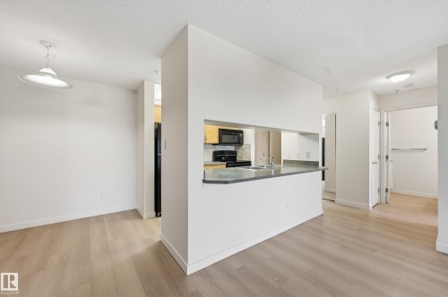 Open-concept living space featuring wood-finish flooring, a kitchen pass-through with a breakfast bar, recessed lighting, and a contemporary pendant light fixture - 314 2430 Guardian Road, Edmonton, AB 
