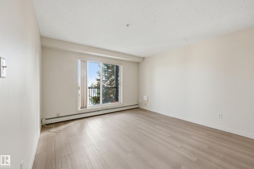 Bright room featuring light wood-finish flooring and a sliding glass door opening to a balcony with black railings - 314 2430 Guardian Road, Edmonton, AB 
