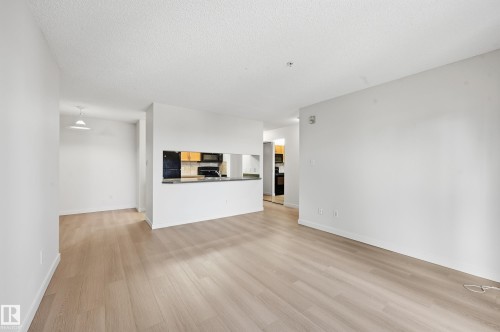 Open-concept living area featuring light wood-finish flooring, white walls, and a pass-through window to the kitchen - 314 2430 Guardian Road, Edmonton, AB 