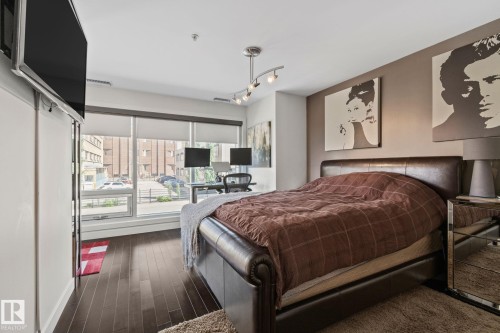 Room featuring dark wood-finish flooring and a full-wall window with roller shades - 201 10388 105 Street, Edmonton, AB 