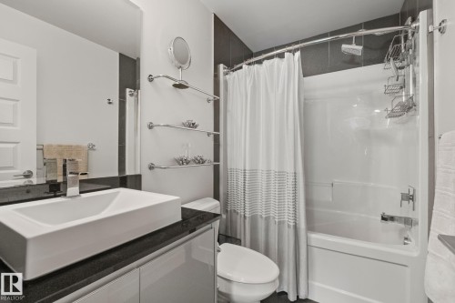 Modern bathroom featuring a rectangular vessel sink, dark countertop, white vanity cabinetry, built-in tub with shower, and chrome fixtures - 201 10388 105 Street, Edmonton, AB 