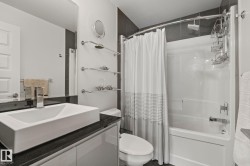 Modern bathroom featuring a rectangular vessel sink, dark countertop, white vanity cabinetry, built-in tub with shower, and chrome fixtures - 