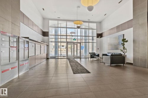 Spacious lobby featuring a soaring ceiling, floor-to-ceiling windows, large format tile flooring, and contemporary overhead lighting fixtures - 201 10388 105 Street, Edmonton, AB 