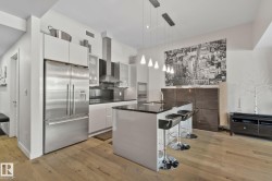 Modern kitchen featuring stainless steel appliances, a center island with pendant lighting, dark countertops, white cabinetry, and wood-finish flooring - 