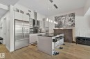 Modern kitchen featuring stainless steel appliances, a center island with pendant lighting, dark countertops, white cabinetry, and wood-finish flooring - 201 10388 105 Street, Edmonton, AB 